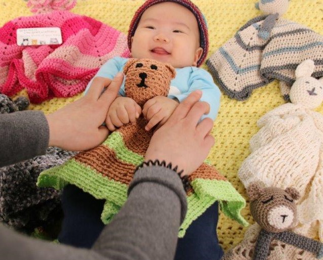 A smiling baby surrounded by knitting holding hands with parent