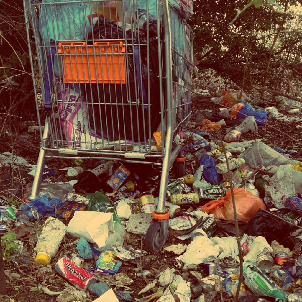 A shopping cart surrounded by rubbish and cans