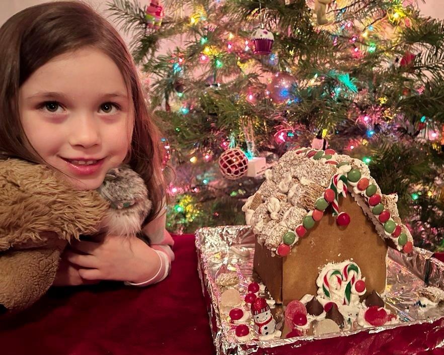 Girl posing next to a gingerbread house with a Christmas tree in the background