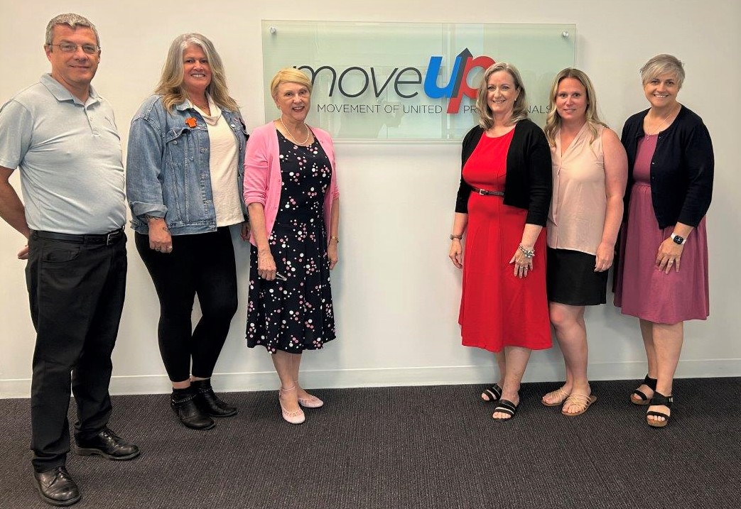 MoveUP Secretary-Treasurer Graeme Hutchison, MoveUP Vice-President Rysa Kronebusch, Parliamentary Secretary for Labour Janet Routledege, MoveUP President Lori Mayhew, MoveUP Vice-President Christy Slusarenko, and MoveUP Vice-President Annette Toth pose in front of a MoveUP sign.