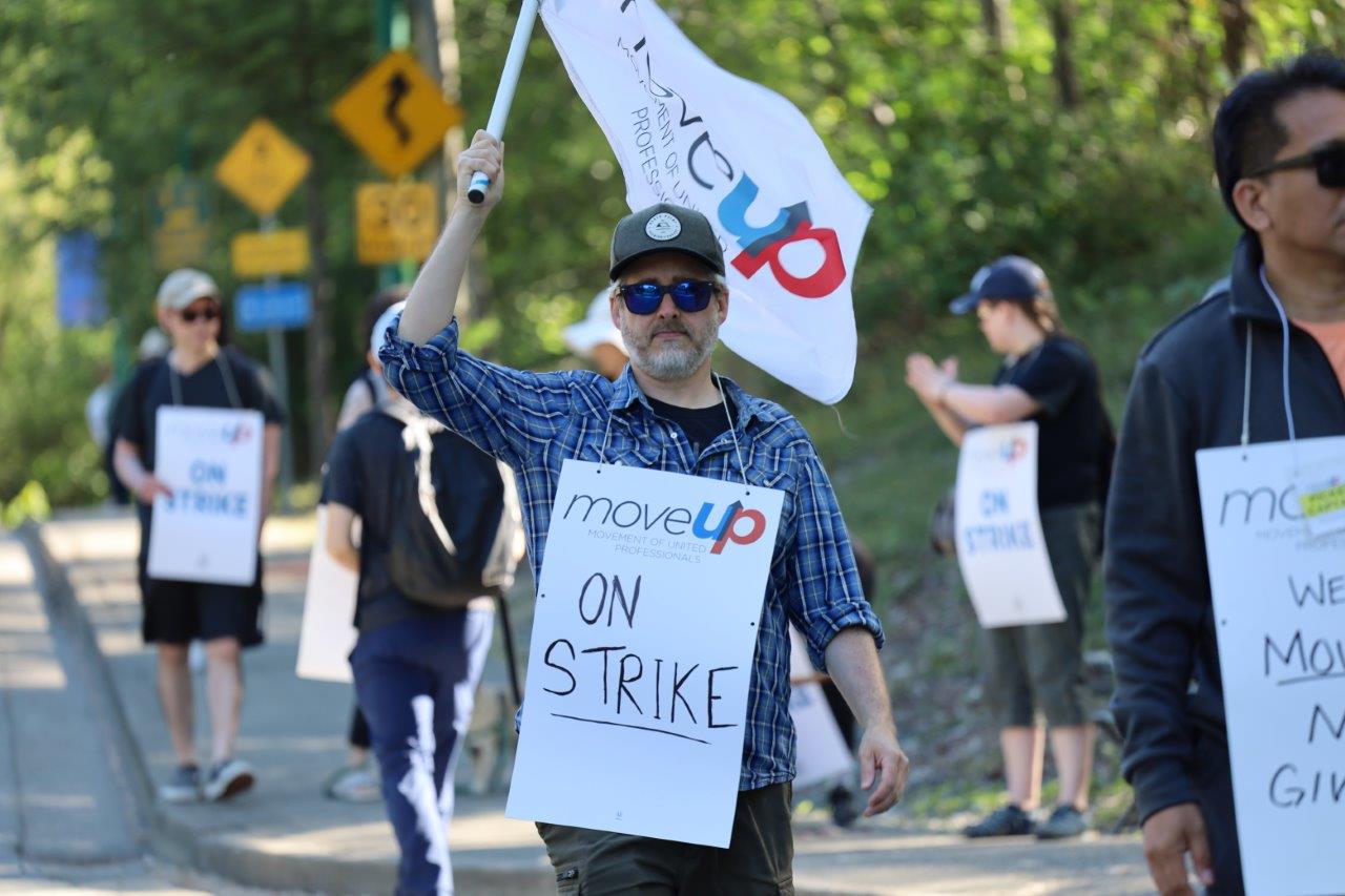 MoveUP member wearing a picket sign and holding up a MoveUP flag