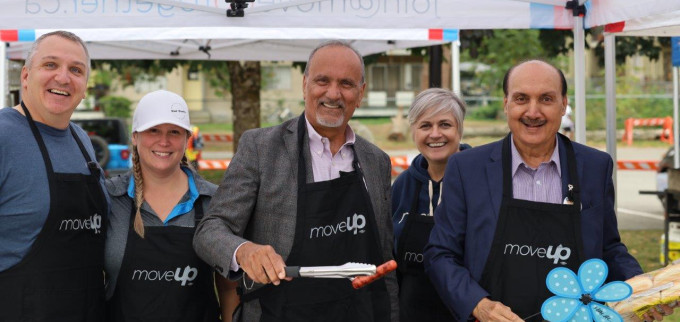 MoveUP leadership (Brian Martens, Christy Slusarenko and Annette Toth) stand with Minister Harry Bains and Speaker Raj Chouhan underneath a MoveUP tent behind a barbecue grill wearing MoveUP aprons