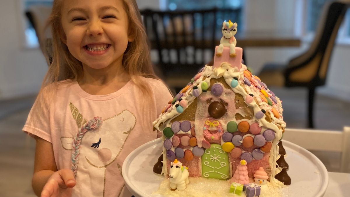Avery smiling while posing next to her gingerbread house