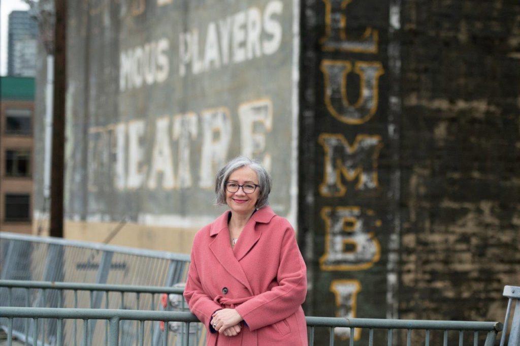 Jennifer Whiteside dressed in pink coat in front of building with the word "Theatre" on it