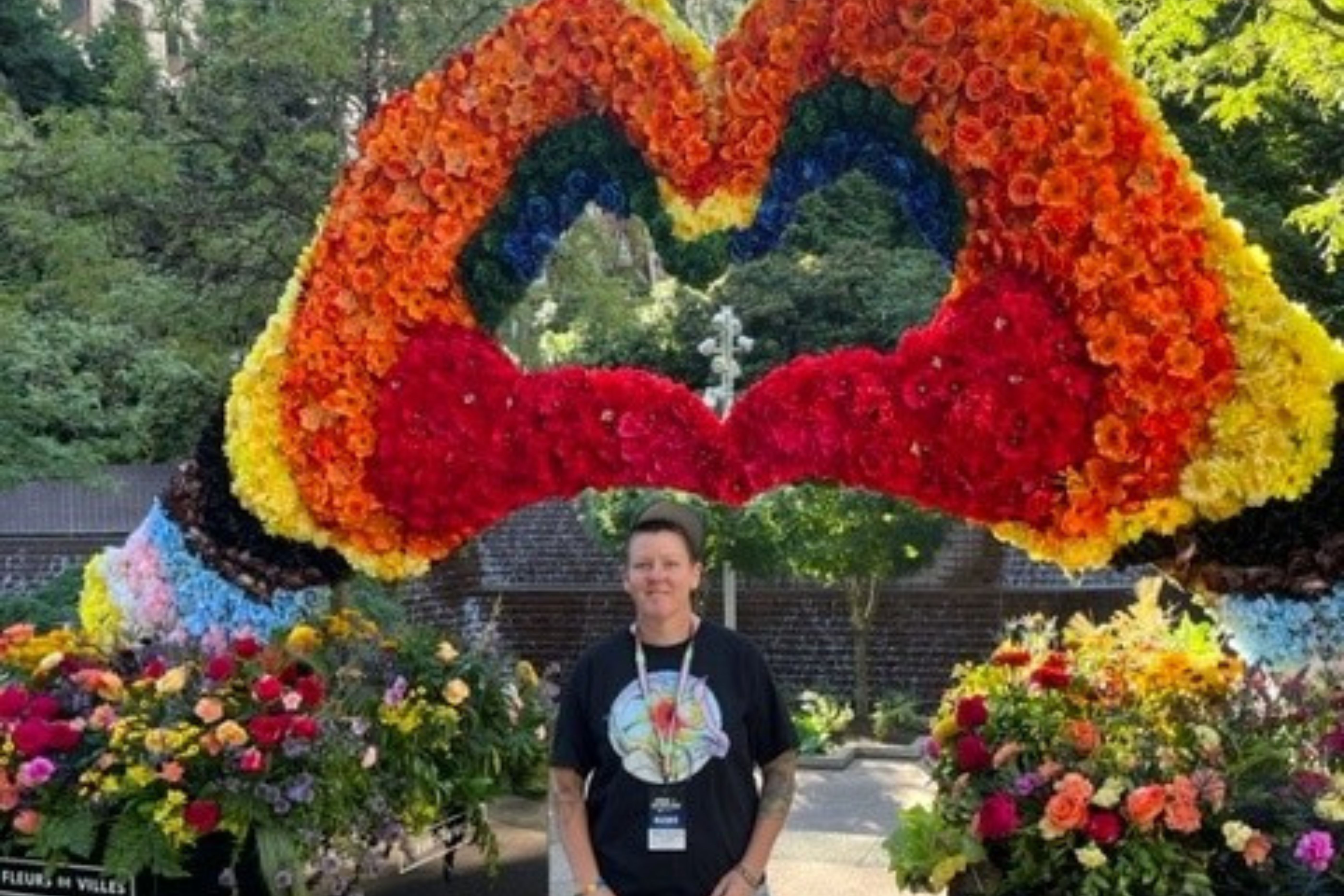 Person poses in front of floral arrangement made to look like two hands making the shape of a heart