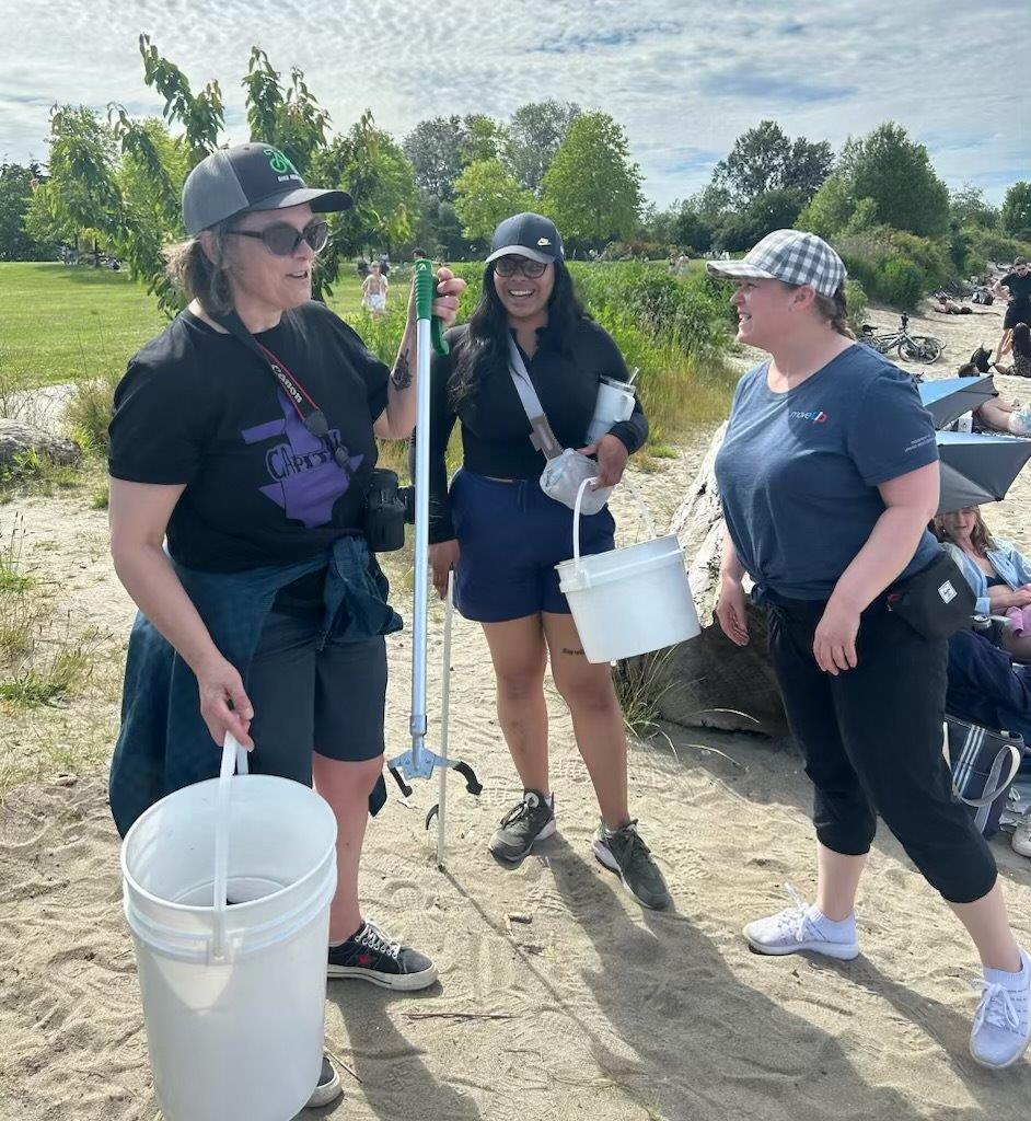 Three people on a beach holding cleanup tools