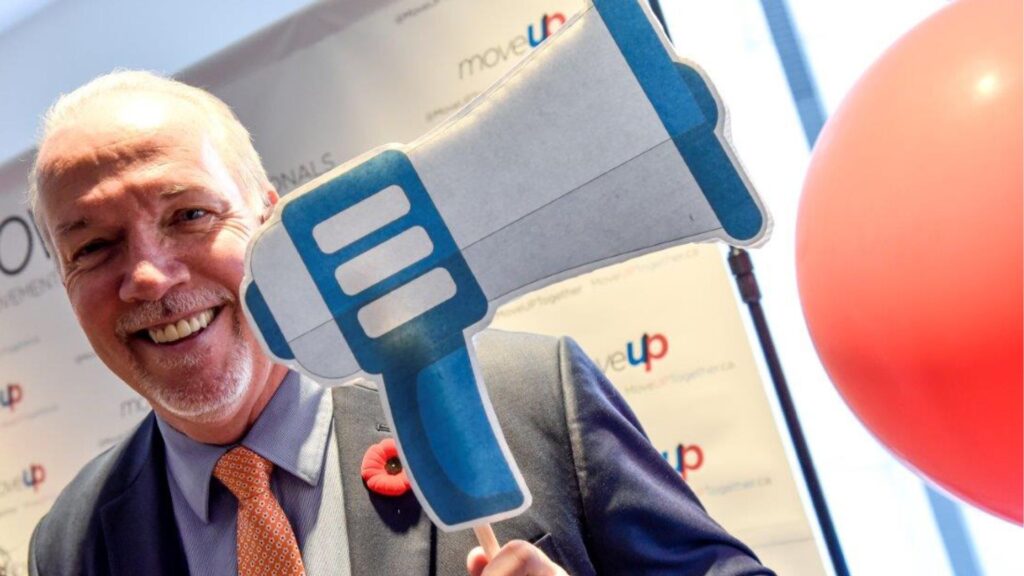 Former BC Premier John Horgan holds up a prop megaphone with a MoveUP backdrop in the background