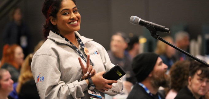 MoveUP member flashes a peace sign while standing at a microphone at the BCFED Convention