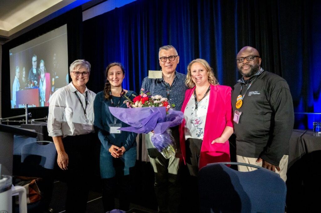 MoveUP member holding flowers while accepting award joined on stage by peers