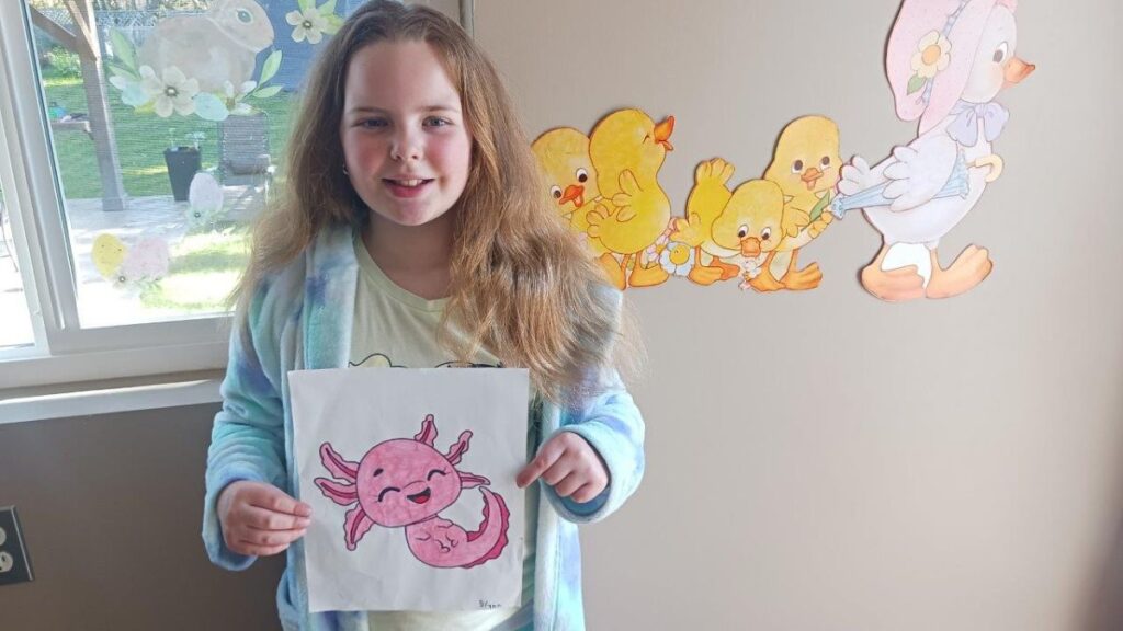 Young girl holding up coloured drawing of sea creature