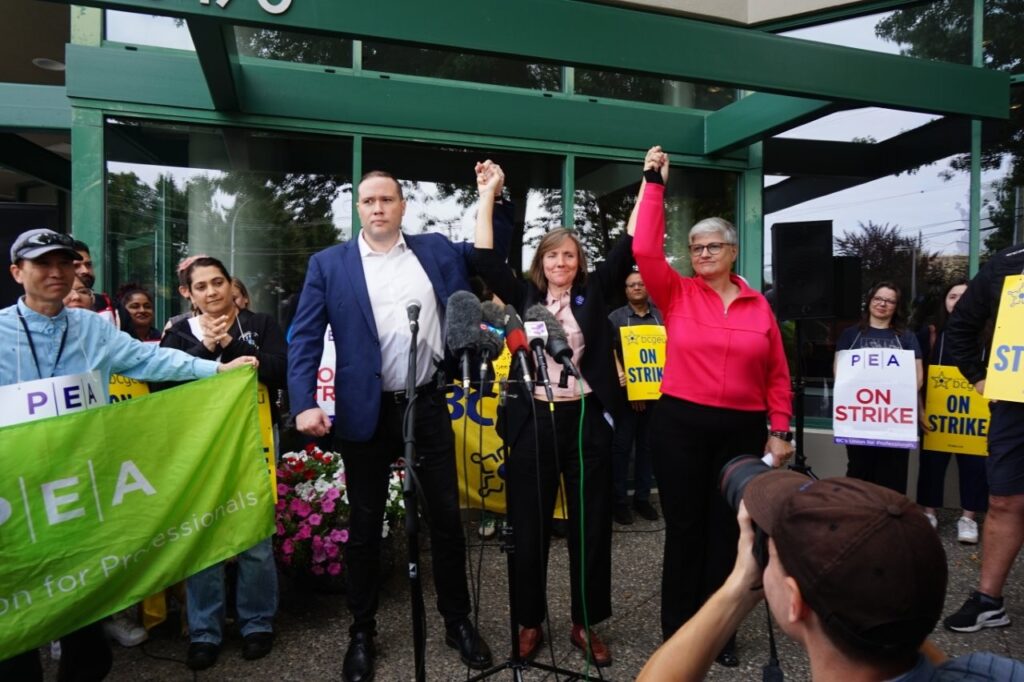 MoveUP President Annette Toth (right) raises her arms with PEA Executive Director Melissa Moroz and BCGEU President Paul Finch