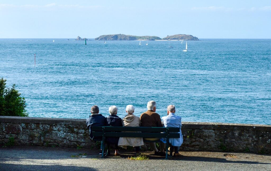 senior citizens sitting on a park bench next to ocean